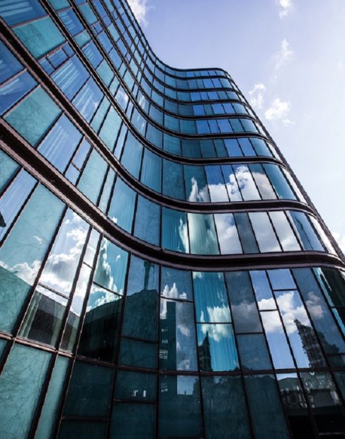 A vertical low angle shot of a high rise building in a glass facade with the reflection of the surrounding buildings