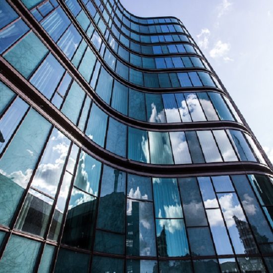 A vertical low angle shot of a high rise building in a glass facade with the reflection of the surrounding buildings